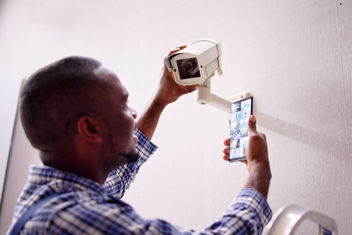 A man using a cell phone to monitor home security through a camera system.