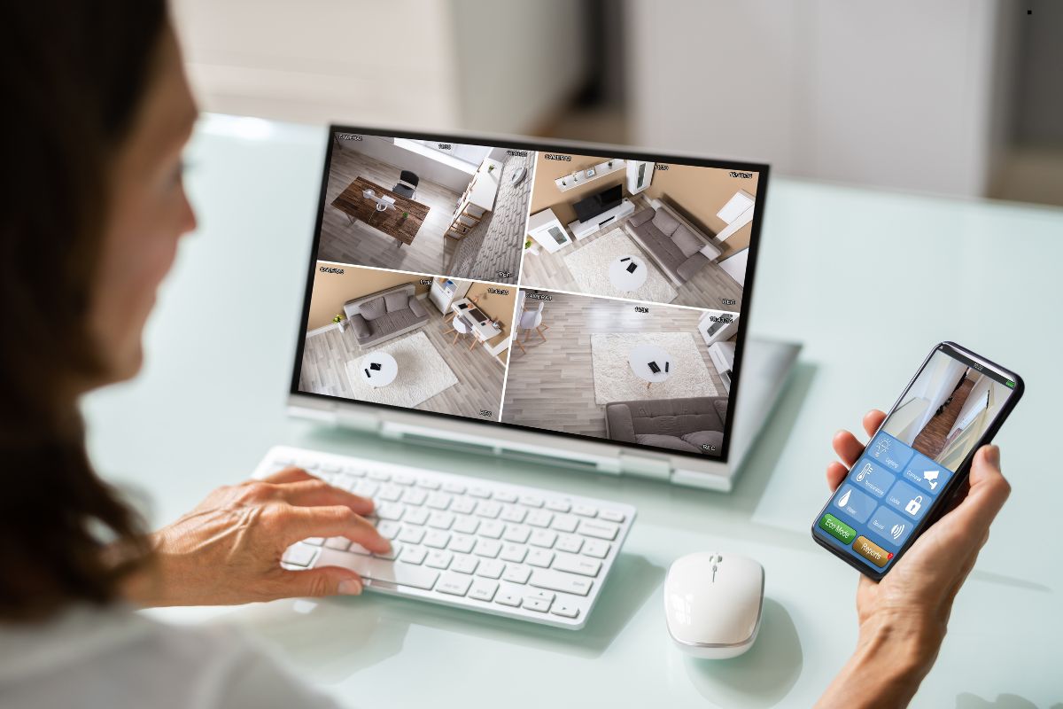 A woman watches a video on her computer while using her phone, highlighting home security services.